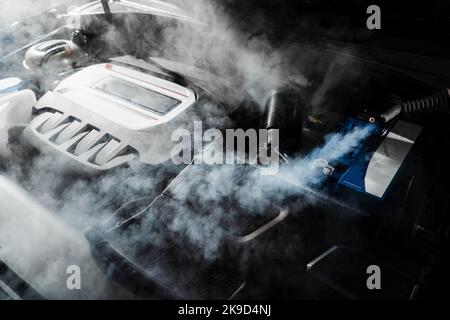 Processo di pulizia a vapore del motore dell'auto da polvere e sporcizia. Lavaggio a vapore del motore di auto nei dettagli del servizio auto Foto Stock