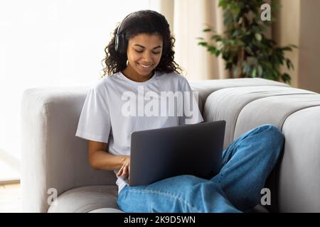 Giovane ragazza afroamericana hipster in auricolare utilizzando un computer portatile parlare con la webcam con un amico on-line videochiamata Foto Stock