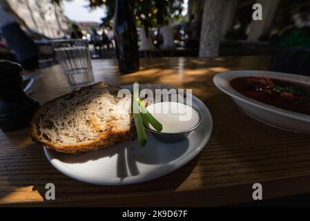 Vista ravvicinata fette di pancetta affumicata con pane nero integrale di segale, cipolla verde e panna acida sul tavolo. Foto Stock