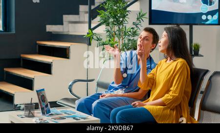 Infermiera femminile e paziente asiatico che guarda all'ologramma futuristico, utilizzando la realtà aumentata e l'immagine olografica alla consultazione in sala d'attesa. Analisi dei 3D ai ad alta tecnologia al momento del controllo. Foto Stock
