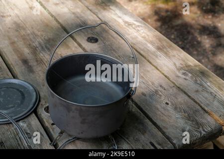 Una pentola di titanio per preparare il cibo su una stufa a gas su un tavolo da campeggio in legno nella foresta. Foto Stock