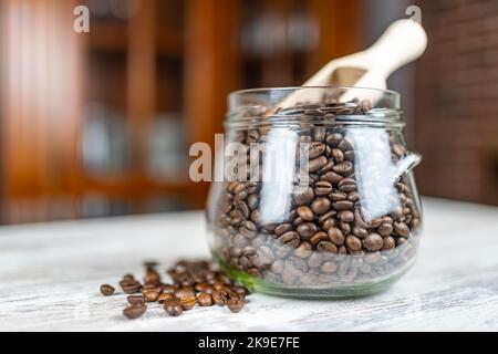 Chicchi di caffè tostati naturalmente in un antico vaso di vetro e cucchiaio di legno per raccoglierli. Foto Stock