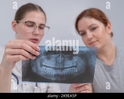 Una dottoressa e un paziente alla reception stanno discutendo di una radiografia della mandibola. Foto Stock