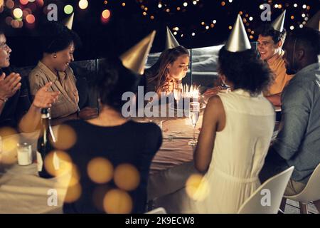 La ragazza di compleanno che fa la sua cosa. Una bella giovane donna che soffia alle candele sulla sua torta di compleanno in una riunione serale con gli amici. Foto Stock