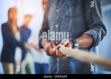 Un gruppo irriconoscibile di uomini d'affari che tirano insieme una corda durante una battaglia di guerra sul lavoro. Foto Stock