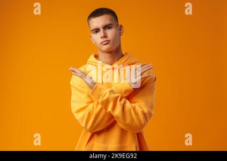 Bel giovane uomo su sfondo giallo che attraversa le braccia facendo segno negativo Foto Stock