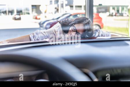 Donna eccitata che abbraccia la sua nuova auto rossa da sogno in una concessionaria di auto. Foto Stock