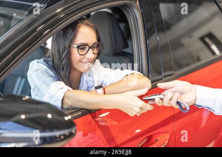 Donna felice che riceve le chiavi della sua nuova auto rossa dal venditore. Foto Stock