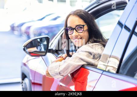 Buona donna di vendita dell'automobile che osserva seduto in una nuova automobile e che guarda la macchina fotografica. Foto Stock