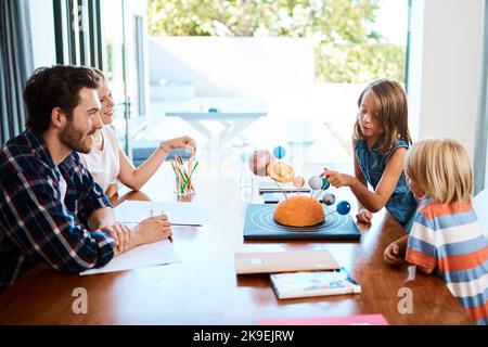 Shes insegnare agli adulti alcune cose. Una bella giovane famiglia che lavora insieme a un progetto di scienza in casa. Foto Stock