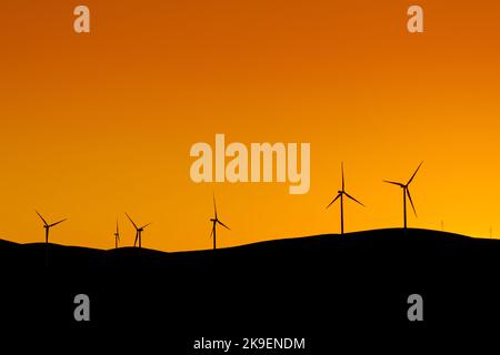Turbine eoliche multiple in piedi su una collina al tramonto e che generano elettricità Foto Stock