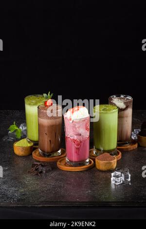 milkshake dolci con cioccolato, caramello, fragola e panna montata su un asse di legno sullo sfondo del tavolo. Foto Stock