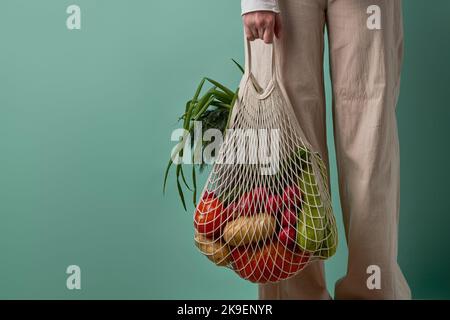 Donna tenere borsa a rete con verdure ed erbe. Shopping moderno riutilizzabile, stile di vita ecologico, concetto di zero sprechi. Foto Stock