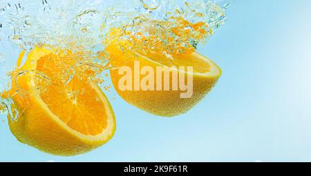 Arance che cadono in acqua con spruzzi su sfondo blu Foto Stock