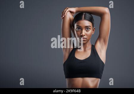 Supera i tuoi limiti. Studio di una giovane donna sportiva che allunga le braccia su uno sfondo grigio. Foto Stock