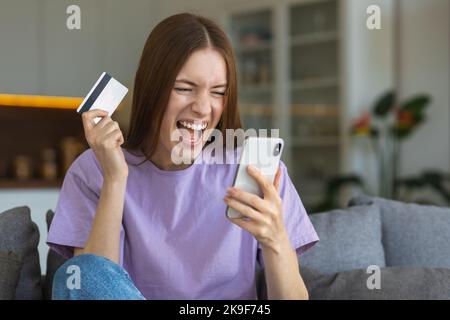 Bella donna piacevolmente eccitato shopping online utilizzando il telefono cellulare. Felice donna sorridente che tiene la carta di credito Foto Stock