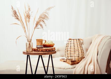 Cozycore o Cottagecore concetto, caldo marrone morbido beige interni oggetti di design. Accogliente plaid di lana sul divano, candela in lanterna di legno, tè tazza. Foto Stock