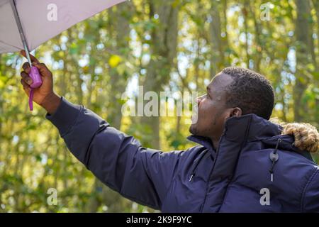 ritratto di un giovane africano con un ombrello in natura. moda invernale Foto Stock