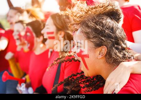 Tifosi di sport rossi multirazziali urlano mentre sostengono la loro squadra - tifosi di calcio che si divertono all'evento di competizione - Focus on african Girl Face Foto Stock