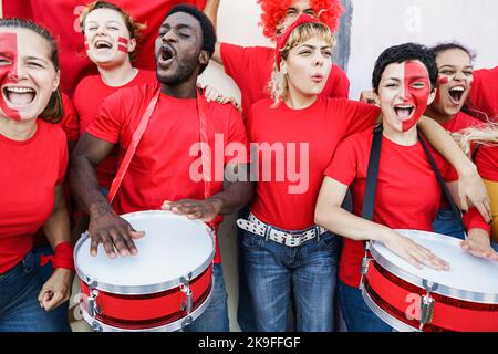 Tifosi di sport rossi multirazziali urlano mentre sostengono la loro squadra - tifosi di calcio che si divertono durante l'evento di competizione - Focus sulla faccia destra ragazza Foto Stock