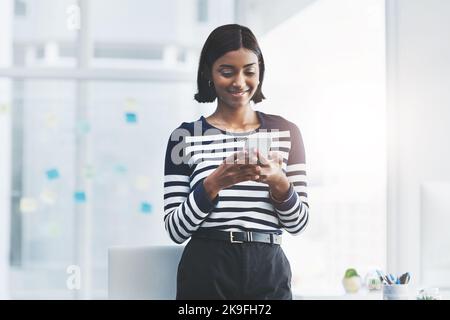 La sua sempre buona udito da voi. Una giovane donna d'affari in piedi e utilizzando il suo cellulare in ufficio. Foto Stock