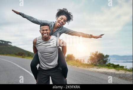 Le dà le ali. Ritratto corto di un bel giovane sportivo piggybacking la sua giovane ragazza atletica fuori. Foto Stock