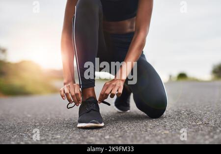 Preparati a correre nel mondo. Primo piano di una donna sportiva che legava le scarpe mentre si allenava all'aperto. Foto Stock