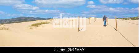 Uomo che cammina sulla bella vista delle tipiche dune di sabbia sulla spiaggia di Guincho, situata a Sintra, Portogallo. Foto Stock