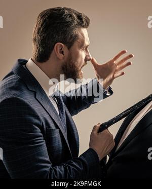 Aggressivo avvocato in tuta fare minacciare gesto tirando uomo cravatta sfondo grigio, minaccioso Foto Stock