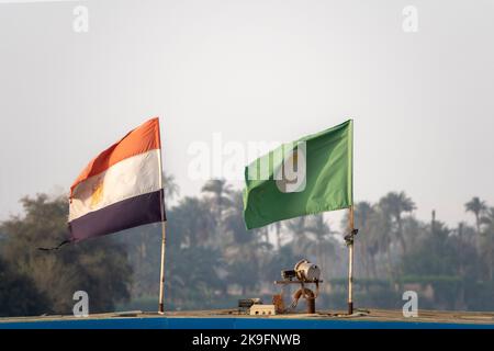 Bandiere che volano dalla parte superiore della cabina di una delapidated nave da crociera con le palme di fuoco molle in lontananza Foto Stock
