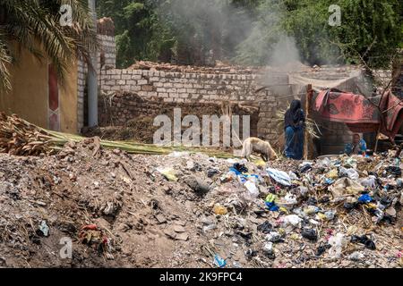 Rifiuti domestici generali e rifiuti scaricati sulla riva del fiume lungo il Nilo con due donne e un cane vicino Foto Stock