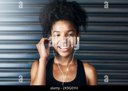 Pensi che positivo e positivo verrà. Ritratto di una giovane donna sportiva che ascolta musica mentre si esercita su uno sfondo grigio. Foto Stock