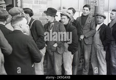 1938, storici, lavoratori industriali in coda fuori dal loro posto di lavoro per il salario settimanale, Treforest Industrial Estate, Rhondda, Galles del Sud, Regno Unito. Le origini della tenuta sono la South Wales & Monmouthshire Trading Estates Ltd, una società governativa senza scopo di lucro fondata per creare e diversificare l'occupazione nella zona, lontano dalle tradizionali industrie del carbone e dell'acciaio che erano in declino a lungo termine. A metà degli anni '1940s, circa 16.000 persone erano occupate nella proprietà commerciale. Foto Stock