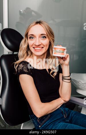 Una donna sulla sedia di un dentista tiene una mandibola con bretelle nelle sue mani Foto Stock