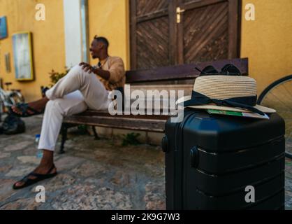 Un buon maschio nero sta sedendo su una panchina e ridendo. Aspetta che la sua ragazza torni Foto Stock