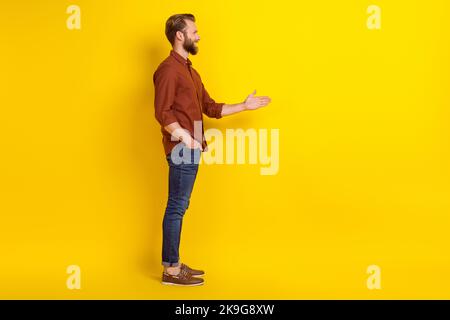 Profilo laterale foto di soddisfatto ottimista positivo uomo borgogna camicia guardare spazio vuoto dare handshake isolato su sfondo di colore giallo Foto Stock