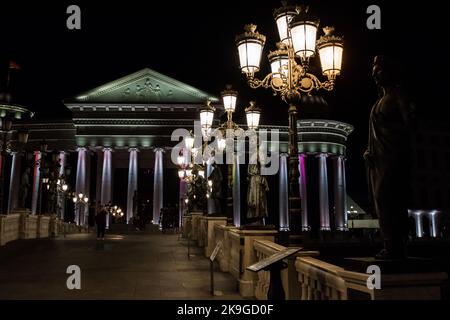 Statue che decorano il Ponte delle civiltà, di fronte al Museo Archeologico di Skopje, Macedonia settentrionale. Di notte con lampioni che illuminano il ponte. Foto Stock