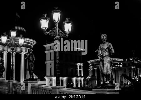 Statue che decorano il Ponte delle civiltà, di fronte al Museo Archeologico di Skopje, Macedonia settentrionale. Di notte con lampioni che illuminano il ponte. Foto Stock