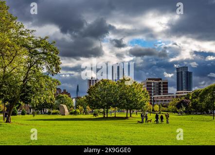 Londra ha molti spazi aperti come questo confinante con la City of London.Shoreditch Park visto qui guardando verso nuvole e grattacieli minacciosi Foto Stock