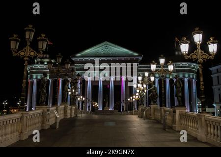 Statue che decorano il Ponte delle civiltà, di fronte al Museo Archeologico di Skopje, Macedonia settentrionale. Di notte con lampioni che illuminano il ponte. Foto Stock