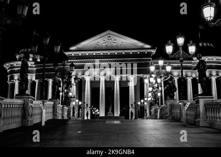 Statue che decorano il Ponte delle civiltà, di fronte al Museo Archeologico di Skopje, Macedonia settentrionale. Di notte con lampioni che illuminano il ponte. Foto Stock