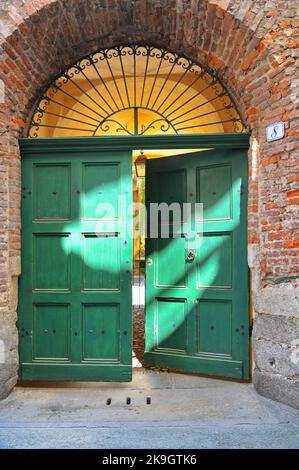 Un antico portale in legno verde e ferro battuto su pareti rustiche in mattoni rossi Foto Stock