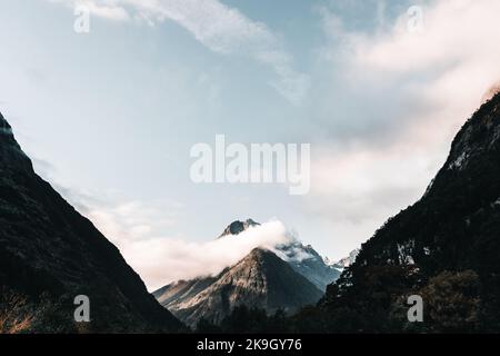 splendido paesaggio di calme montagne rocciose innevate tra nuvole e cielo blu, milford sound, nuova zelanda Foto Stock