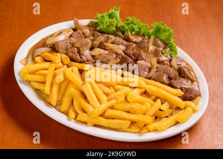 Filetto mignon con patatine fritte, servito in stile brasiliano su tavolo di legno. Foto Stock