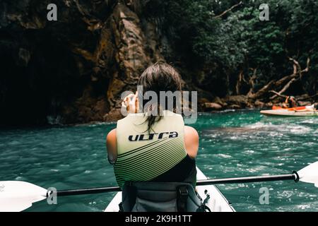 ragazza caucasica con i capelli sporchi dal retro scattando una foto delle rocce seduti sul kayak nell'isola di ciambelle, nuova zelanda Foto Stock