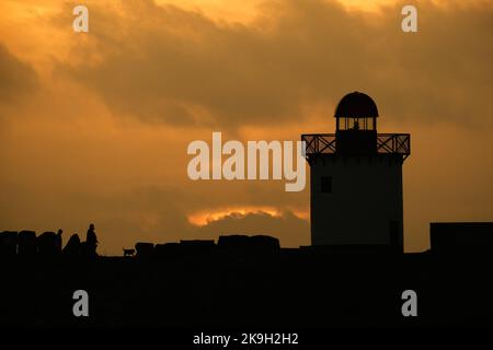 Bury Port, Carmarthenshire, Regno Unito. 28th ottobre 2022. Meteo nel Regno Unito. Camminare con il cane: Un ultimo assaggio del sole per questo canino e i suoi proprietari dopo una giornata nuvolosa nella piccola cittadina balneare di Burry Port, Carmarthenshire. Il faro del porto è stato eretto nel 1842 sul frangiflutti ovest a Burry Port. Si affaccia sulla foce del Burry Inlet, un estuario tra la penisola di Gower e la costa del Carmarthenshire. Credit: Gareth Llewelyn/ Alamy Live News Foto Stock