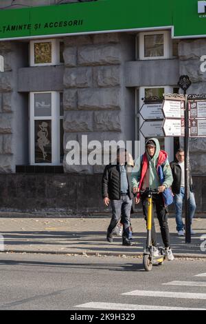 Chisinau, Moldova - 15 ottobre 2022: Un giovane uomo attraversa un passaggio pedonale su uno scooter elettrico, fuoco selettivo. Foto Stock