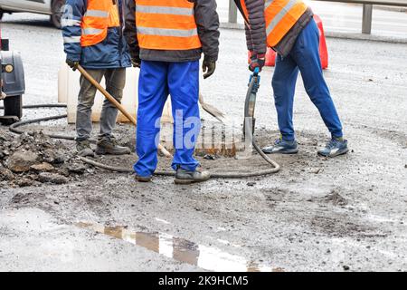 Un team di lavoratori della strada rimuove l'asfalto vecchio intorno a un tombino della fogna con un martello e una pala per una riparazione successiva. Spazio di copia. Foto Stock