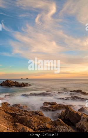 Una fotografia mozzafiato cattura la bellezza di una costa rocciosa bagnata dal caldo bagliore del sole che tramonta. Foto Stock