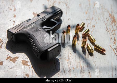 Una pistola semi-automatica da 9mm Glock 19, realizzata in Austria, appoggiata su un tavolo di legno, insieme ad un gruppo di 9mm proiettili. Foto Stock